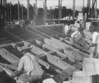Placing the north aisle roof of the nave. The original roof, assembled in the carpenter shop, was destroyed by fire in 1916, and this new roof was made ready in months of hand labor. The man in the foreground is sawing off the protruding end of locust wood pegs used to fasten purlins and rafters together.